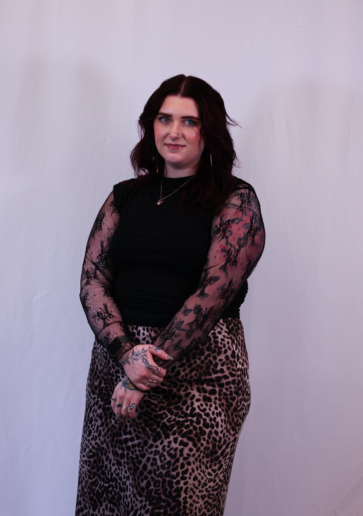 Jessicah facing the camera, wearing a black top and animal-print skirt with hands crossed in front.